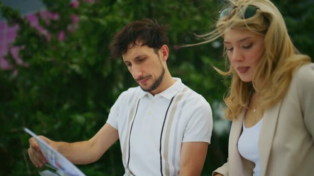 Two business people review documents and charts together in an outdoor setting. They collaborate and analyze important reports with focus.