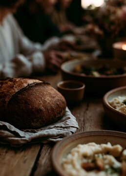Wooden table with several bowls of food on it. on the left side of the table, there is a loaf of bread on a white cloth napkin. the bread appears to be freshly baked and has a golden brown crust.
