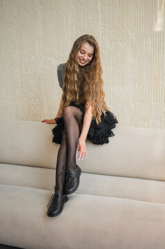 Young woman with long wavy hair sitting on sofa smiling downwards in textured neutral interior, with woman, smile, hair, longhair detail, showing wavyhair, seated, sofa, couch context