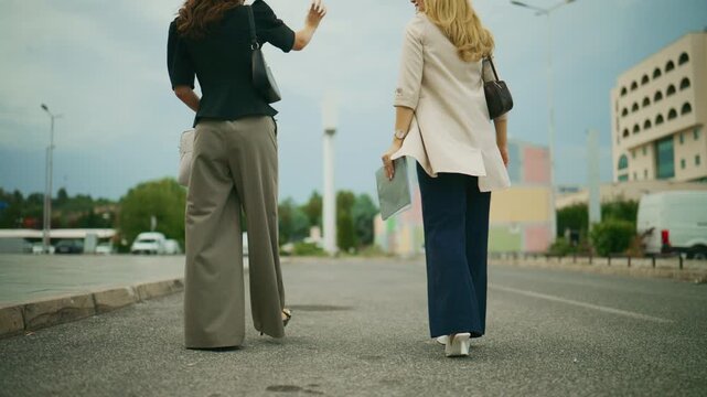 Two professional business people are seen walking and then stopping to discuss work outdoors. They are reviewing documents and a tablet in an urban setting, engaged in a conversation.