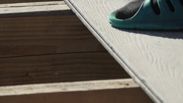 Hammer striking composite decking board to secure joints onto wooden frame during outdoor home improvement. Extreme close-up shot.