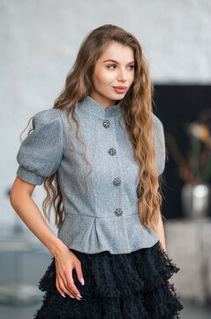 Young woman in gray buttoned jacket with long wavy hair looking aside in indoor setting, with woman, portrait, fashion, jacket detail, showing button, skirt, hair, wavy context