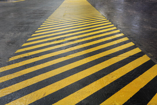 Yellow and black warning stripes on asphalt create impression of safety corridor stretching into distance. Yellow and black hazard stripes painted on dark asphalt