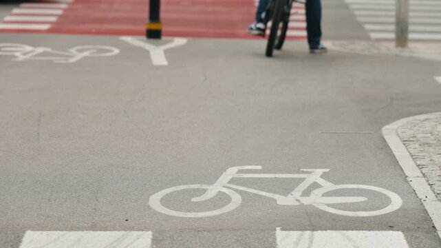 Cyclist riding through an urban bike lane toward a city street, with clear bicycle symbols, red pavement and dedicated road markings illustrating modern cycling infrastructure