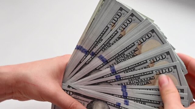 Close up video of hands holding and fanning out stack of new one hundred dollar bills on a white background, showcasing crisp currency texture and movement.