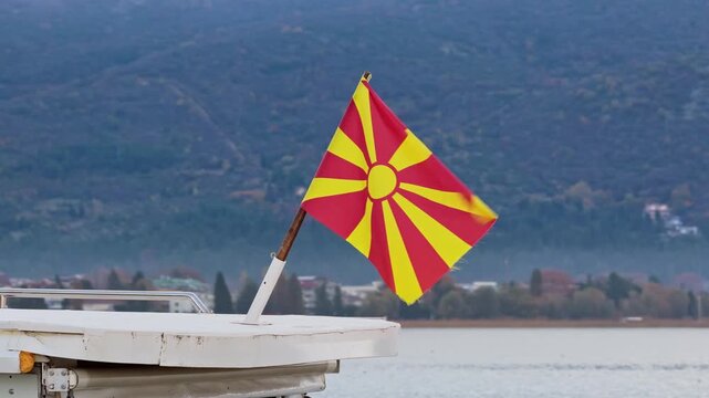 Flag of North Macedonia waving on a boat mast against a scenic mountain lake background.