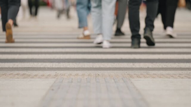 Cinematic close up view urban crosswalk with zebra stripes on asphalt, pedestrians walking in slow motion, cropped legs to knee level, overcast cloudy city atmosphere