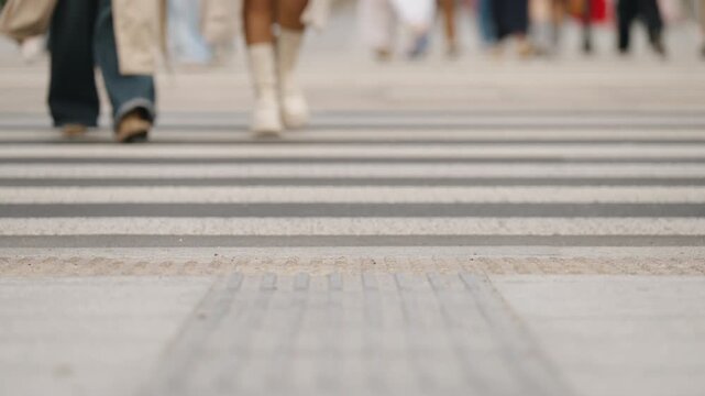 Cinematic close up view urban crosswalk with zebra stripes on asphalt, pedestrians walking in slow motion, cropped legs to knee level, overcast cloudy city atmosphere