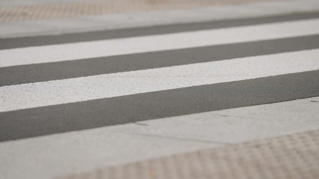 Cyclist riding across marked pedestrian zebra crossing in slow motion, close-up view of bicycle wheels moving over white road markings, urban traffic infrastructure and road safety