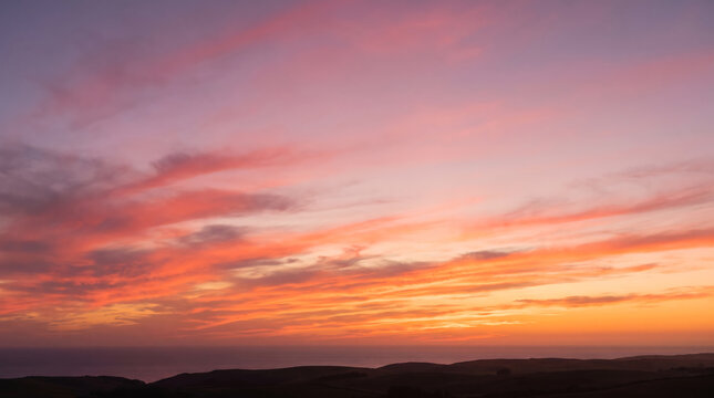 Vibrant orange and pink sunset sky over distant rolling hills