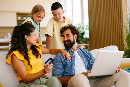 Happy family together on a sofa, parents and children enjoying online shopping at home, using a laptop and holding a credit card for a secure purchase