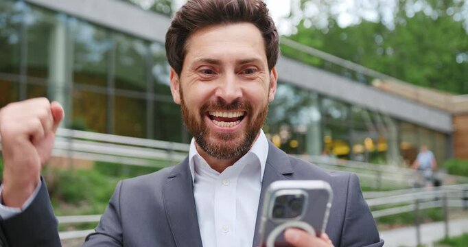 Close-up of a smiling man holding a smartphone and checking email outdoors, expressing happiness and positive emotions while reading a message on a mobile device.
