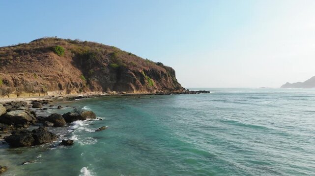 Aerial view drifting along rocky shore with tide pools below coastal cliff at Tanjung Aan Lombok