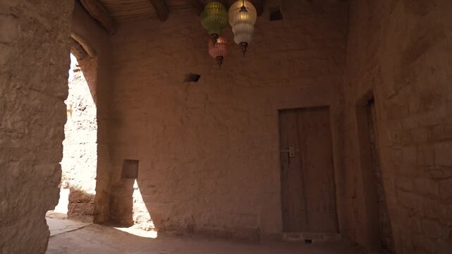 Cinematic low angle interior shot of colorful glass lanterns hanging from wooden palm roof in AlUla Old Town mud house