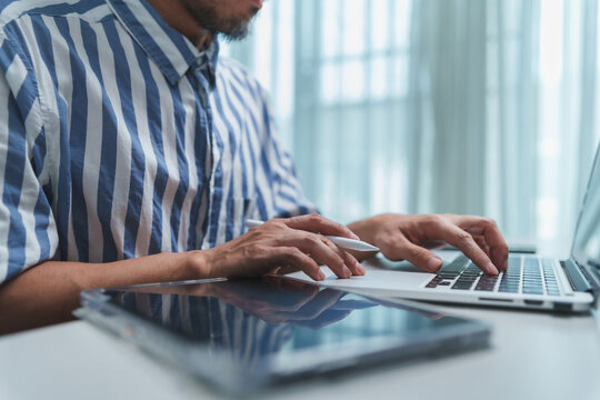 Professional man types on a laptop beside a digital tablet at a modern desk, representing online business, office work, digital technology, creative workflow, communication and work productivity.