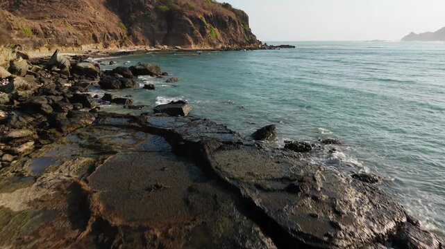 Aerial drone flight over eroded coastal rock and tide pools toward open turquoise sea Lombok Indonesia