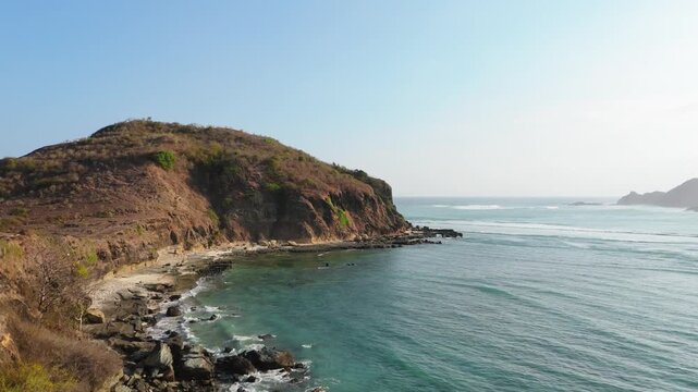Aerial orbit around coastal headland with secluded beach and reef break Kuta Mandalika Lombok