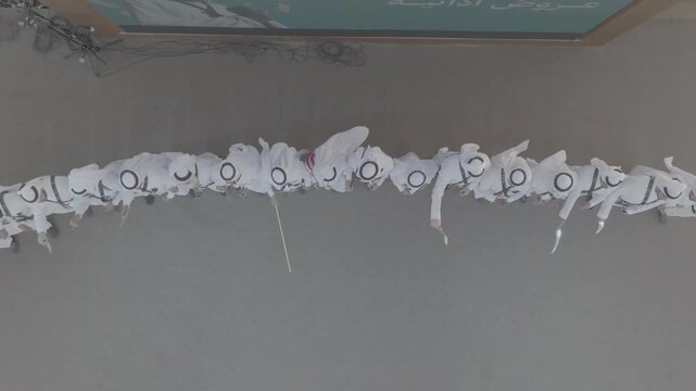 Cinematic top down drone aerial shot of traditional folklore group performing Southern Saudi Ardah dance in white thobes