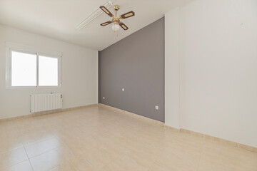 Fototapeta premium Empty room with gray accent wall, ceiling fan, window with radiator, and beige tiled floor