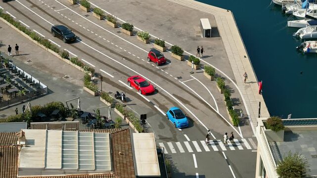 Aerial view of colorful cars driving on road alongside marina in Monaco.
