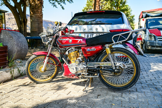 Red Arora CG 50 light motorcycle parked by the roadside in Halfeti; a modified CG-style motorcycle with spoked wheels; Şanlıurfa, Southeastern Anatolia, T&uuml;rkiye 10.09.2025