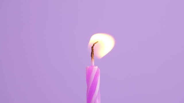 Burning birthday candle with bright flickering flame on soft purple background, minimal festive close-up representing birthday celebration, wishes, anniversary, party, and special occasion