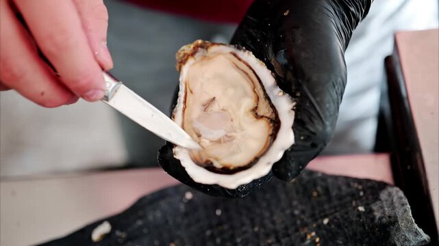 Professional chef hands opening fresh raw oyster with knife close up in slow motion.