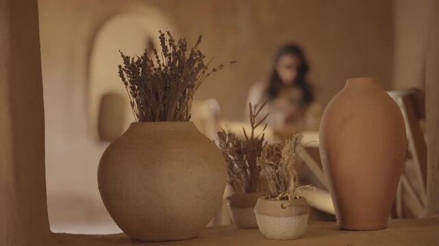 Cinematic close-up of rustic terracotta clay pottery vases filled with dried lavender flowers in peaceful warm indoor lobby decor