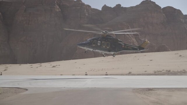 Cinematic shot of luxury chartered helicopter landing smoothly on desert helipad amidst dramatic AlUla sandstone mountains