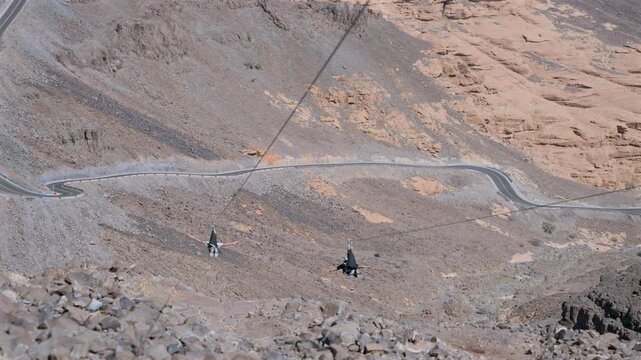 High-angle shot of people ziplining on a fast cable above rocky mountain valley in AlUla