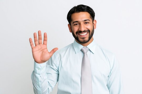 Smiling businessman in light blue shirt and tie waving hand with open palm against white background