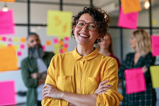 Smiling female entrepreneur with curly hair and glasses standing in creative office space