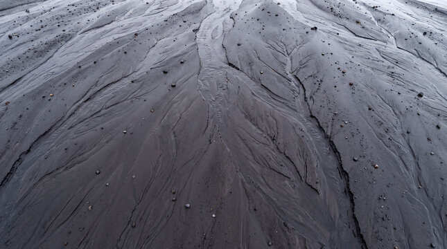 Volcanic ash carved by rain with small stones scattered on dark textured surface creating natural