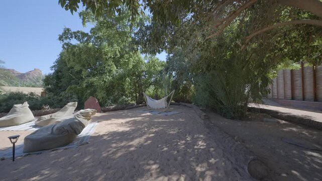 Relaxing shaded outdoor lounge area with hammock and beanbag chairs under trees in AlUla