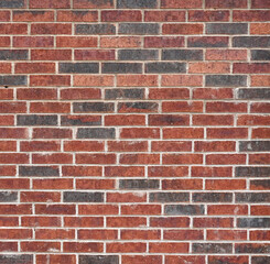 Fototapeta premium Horizontal close up of a red brick wall surface with scattered black bricks, variegated bricks and a rough brick texture with porous even white mortar 