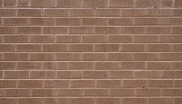 A terra cotta painted brick wall with rough grooved brick faces, porous mortar, chipped paint around a protruding nail, and scattered paint loss along the joints in a horizontal close‑up view