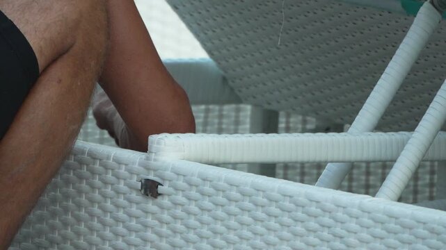 Maintenance worker tightening strings on white wicker sunbed at resort terrace. Close-up static shot.