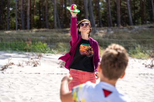 Woman Playing Paddle Ball With Child On Beach During Summer Family Vacation And Recreation