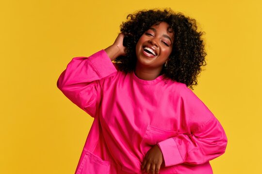 Cheerful woman in pink clothing smiling on a vivid yellow background in studio