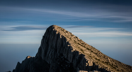 Fototapeta premium Striking rocky mountain peak under a clear blue sky, illuminated by golden sunlight, emphasizing the dramatic and awe-inspiring beauty of a high-altitude wilderness