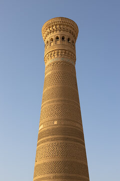 Kalyan Minaret in Bukhara with intricate geometric brickwork bands against a clear blue sky. Ideal for travel guides, heritage publications, and cultural brochures about Uzbekistan and the Silk Road.