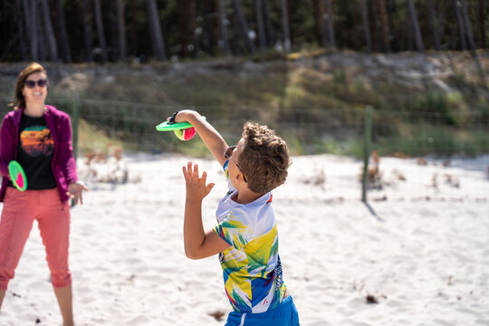 Child Playing Paddle Ball With Woman On Beach During Summer Family Vacation And Outdoor Fun