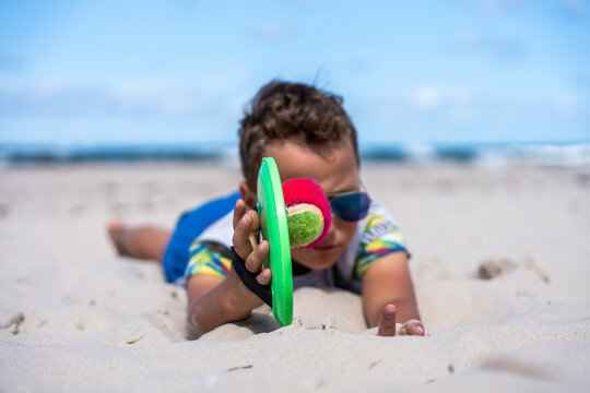 Child Playing Paddle Ball On Sandy Beach During Summer Vacation Outdoor Fun And Recreation