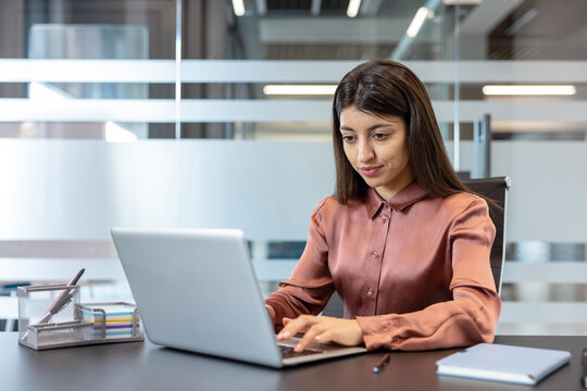 Professional woman typing on a laptop, actively working at a desk in a contemporary corporate office environment, focusing on productivity and business tasks