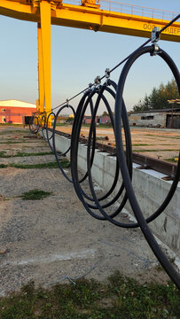 Thick black industrial cables hang from a metal fence in an outdoor yard, construction infrastructure, heavy duty equipment.