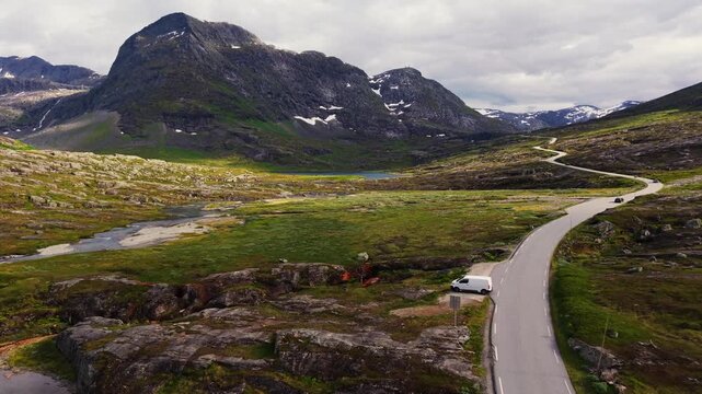 aerial of Trollstigen road winding through a rocky alpine plateau beside turquoise water, lingering snowfields and rugged mountains in western Norway Europe