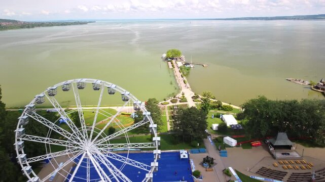 A drone flies forward above the Ferris wheel in Fony&oacute;d, revealing the shoreline of Lake Balaton in Hungary.