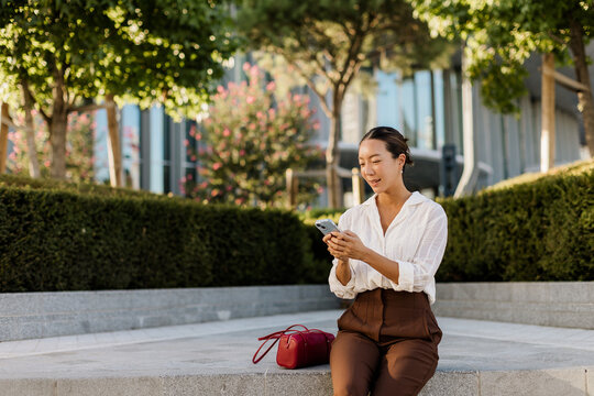 Korean woman enjoying a sunny afternoon while texting in the park garden