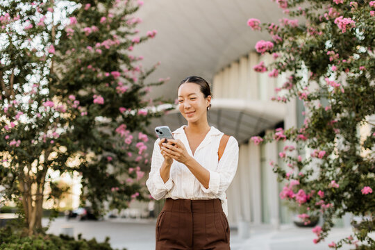 Korean woman enjoys a sunny day while checking her phone among blooming flowers