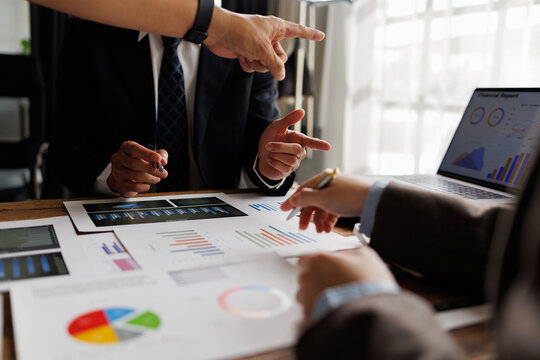 Business professionals collaborate over charts and a laptop, analyzing financial reports, discussing marketing strategy and planning growth during a focused office meeting